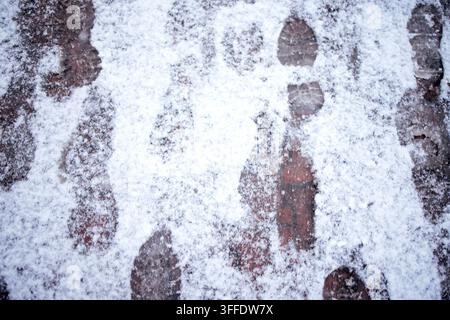 Fußabdrücke sind im frischen Schnee auf einem Ziegelweg sichtbar und unterstreichen eine Winterszene mit einer leichten Schneeschicht, die den Boden bedeckt Stockfoto