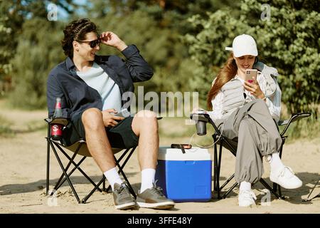 Paar, das in Campingstühlen sitzt und Smartphones im Freien benutzt Stockfoto