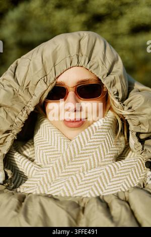 Porträt einer Frau mit Sonnenbrille, die in einem Schlafsack im Freien gewickelt ist Stockfoto