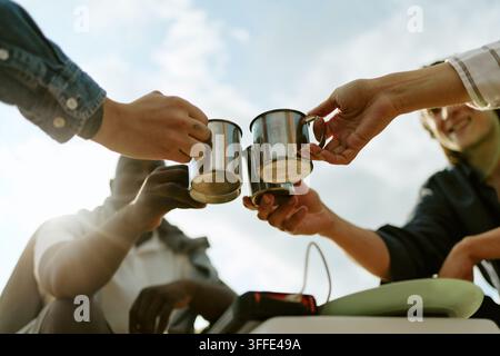 Verschiedene Gruppe von Freunden, die mit Metallbechern im Freien anstoßen Stockfoto
