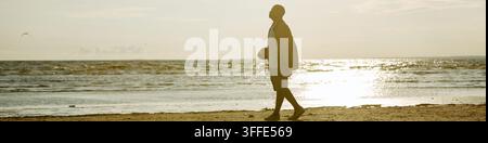 Kopf eines Schwarzen Mannes, der bei Sonnenuntergang am Strandufer einen Fußball hält Stockfoto