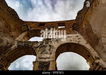 Niedrigwinkelaufnahme antiker Kolosseum-Bögen und Ziegelmauerwerk vor einem dramatischen Himmel in Rom. Stockfoto