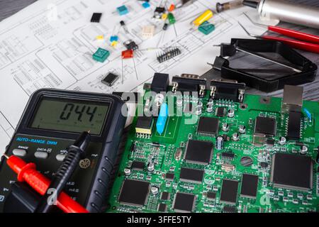 Eine Person testet eine Platine mit einem Multimeter, während verschiedene elektronische Bauteile auf dem Arbeitstisch verstreut liegen. Stockfoto