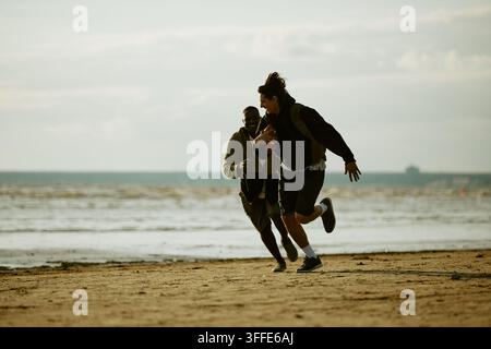 Verschiedene männliche Freunde spielen American Football am Strand Stockfoto