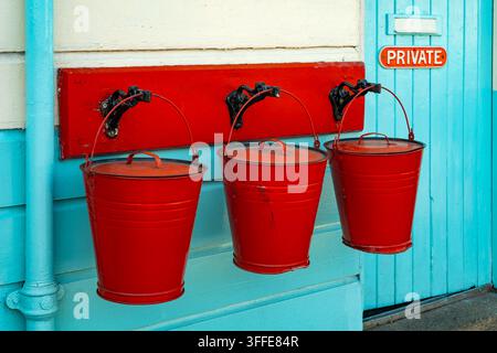 Drei alte rote Feueimädel hängen vor einem türkisfarbenen Holzstationgebäude in Grosmont, North Yorkshire, England. Stockfoto