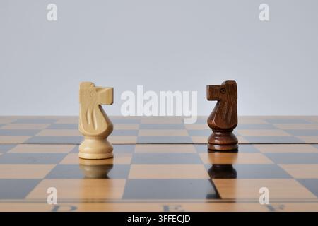 Zwei gegnerische Schachspringer stehen sich auf braunen und beigen Feldern eines glänzenden Holzbretts gegenüber. Die minimale Komposition repräsentiert Wettbewerb, Konfro Stockfoto