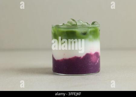Nahaufnahme von gekühltem Ube Halaya Matcha Latte, isoliert auf cremefarbenem Hintergrund. Gesundes veganes Getränk Ube Matcha Latte Stockfoto