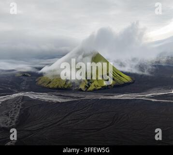 Luftaufnahme des Vulkans Maelifell, der mit leuchtend grünem Moos bedeckt ist, umgeben von weiten schwarzen Vulkansandebenen und tief hängenden Wolken in Skaftarhreppur Stockfoto