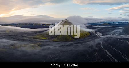 Luftbild des Vulkans Maelifell, der mit leuchtend grünem Moos bedeckt ist, umgeben von tief hängenden Wolken und einer weiten vulkanischen Landschaft in Skaftarhreppur, Island Stockfoto