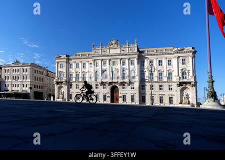 Eine Touristin auf einem Fahrradtrip steht mit ihrem Fahrrad direkt vor dem majestätischen historischen Palazzo del Lloyd Triestino. Stockfoto