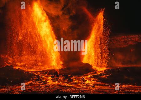 Blick auf mächtige Lavafontänen, die nachts aus dem Kilauea-Krater ausbrechen, mit glühendem geschmolzenem Gestein, das über die dunkle vulkanische Landschaft in Hawaii fließt C Stockfoto