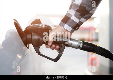 Nahaufnahme eines Mannes, der ein weißes Auto an einer Tankstelle mit Benzin betankt, den Zapfhahn in der Hand, während er Benzin einfüllt Stockfoto