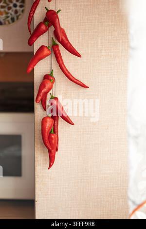 Bündel heißer Chilischoten, die an einer beigen Wand hängen Stockfoto
