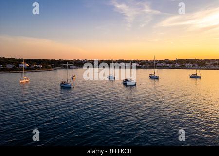 Luftaufnahme von Yachten, die bei Sonnenuntergang vor der ruhigen Küste der Insel Silba, Kroatien, vor Anker liegen. Goldenes Sonnenlicht wärmt das ruhige, tiefblaue Adriatische Meer Stockfoto