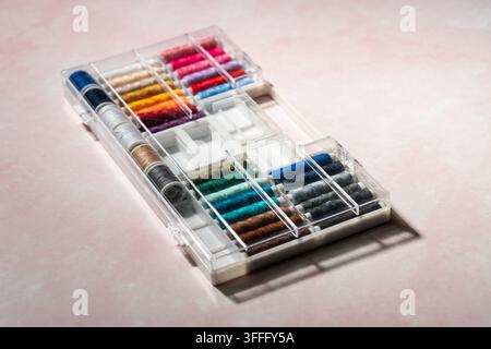 Bunte Nähgarnspulen in einer Schachtel auf rosafrotem Hintergrund arrangiert. Kreatives Textilstillleben, Nähen, Schneiderei, Handwerk, Hobby Stockfoto