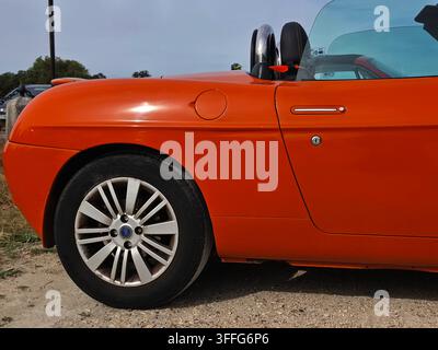 Nahaufnahme im Seitenprofil eines leuchtend orangefarbenen klassischen Fiat Barchetta Roadsters, der die hintere Quartierplatte, das Aluminiumrad und die Chromrollbügel zeigt Stockfoto