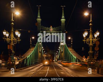 Budapest, Ungarn - 26. August 2026: Nachtansicht der historischen grünen Stahl-Liberty-Brücke, beleuchtet von Straßenlaternen, mit einem herannahenden Publikum Stockfoto