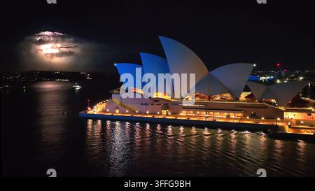 Die ikonische Architektur des Sydney Opera House erhellt die Hafenwässer bei Nacht, während ein dramatischer Gewittersturm im fernen dunklen Himmel über der Stadt blitzt. Australiens Hauptlandmarke, ein Ort, den man besuchen sollte Stockfoto