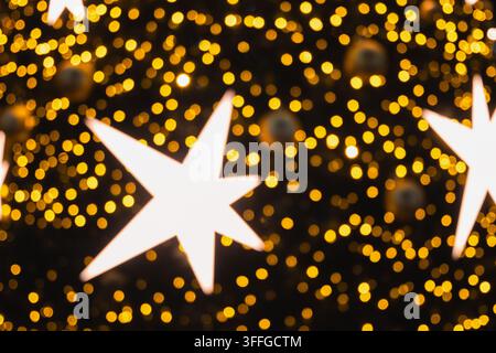 Helle weiße Weihnachtssterne leuchten zwischen unscharf im Hintergrund strahlenden goldenen Lichterketten und schaffen einen abstrakten festlichen Feiertags-Hintergrund und eine warme saisonale Atmosphäre. Stockfoto