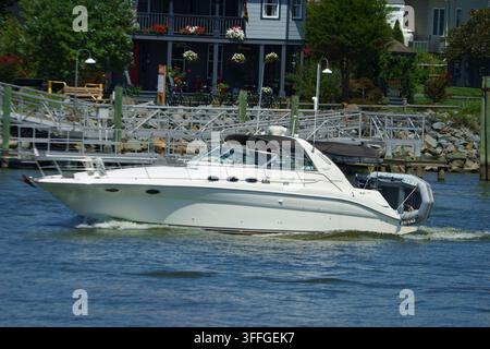 Chesapeake City, MD, USA – 19. August 2022: Ein Boot fährt durch das Wasser neben Häusern mit Blumentöpfen und einem Steg. Es ist Tag, und die Szene scheint Stockfoto