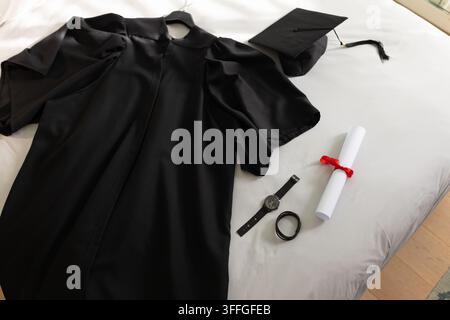 Ein schwarzes Abschlusskleid liegt flach auf weißem Stoff im Fensterlicht, mit Barett Stockfoto