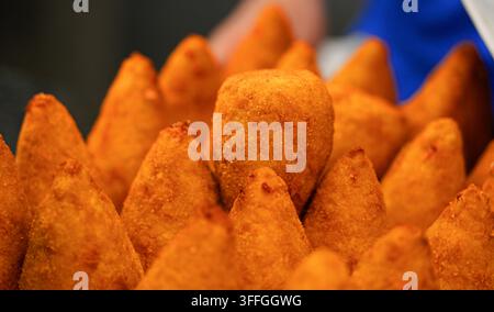 Knusprige italienische Arancini-Reiskugeln. Eine Nahaufnahme von frisch gebratenen, goldbraunen, kegelförmigen italienischen Arancini-Reiskugeln, die aufeinandergestapelt sind. Stockfoto
