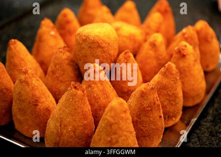 Knusprige italienische Arancini-Reiskugeln. Eine Nahaufnahme von frisch gebratenen, goldbraunen, kegelförmigen italienischen Arancini-Reiskugeln, die aufeinandergestapelt sind. Stockfoto