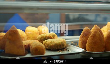Knusprige italienische Arancini-Reiskugeln. Eine Nahaufnahme von frisch gebratenen, goldbraunen, kegelförmigen italienischen Arancini-Reiskugeln, die aufeinandergestapelt sind. Stockfoto