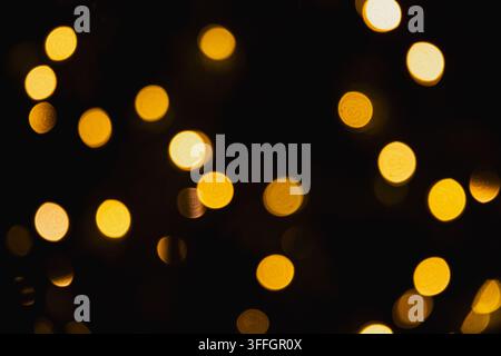 Abstrakte goldene Weihnachtsbokeh-Lichter, die auf dunklem schwarzem Hintergrund leuchten, festliche unscharfe Beleuchtung für Feiertagsdesign mit Kopierraum. Stockfoto