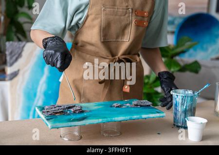 Nahaufnahme einer Künstlerin, die Epoxidharz und strukturierte Details auf einem blauen abstrakten Kunstwerk formt. Stockfoto