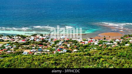 Hohe Blickwinkelansicht des Dorfes Beausejour, des Hafens und des türkisfarbenen Meeres auf der Insel La Desirade in Guadeloupe, Karibik. Stockfoto