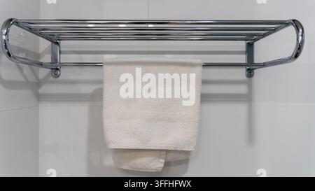 Weißes Handtuch, das an einem Chromregal in einem modernen Hotelbadezimmer hängt Stockfoto