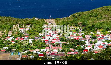 Erhöhte malerische Ansicht von Häusern mit farbenfrohen Dächern im Küstendorf Terre-de-Bas, Les Saintes, Guadeloupe, vor dem blauen Ozean. Stockfoto