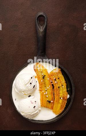 Gebratene Banane mit Eisbällchen in einer Pfanne auf dunklem rustikalem Hintergrund. Köstliches herzhaftes Dessert. Draufsicht, flaches Lay. Stockfoto