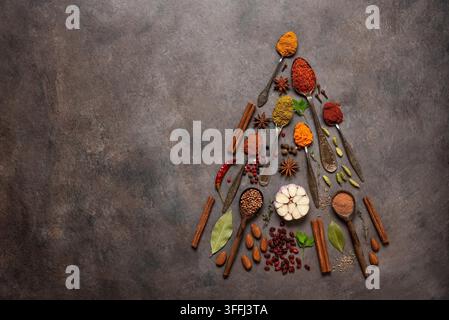 Verschiedene Gewürze in Form eines Weihnachtsbaums auf einem braunen rustikalen Hintergrund. Oberblick, Flat Lay, Kopierraum. Konzept von Weihnachten und Neujahr. Stockfoto