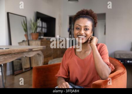 Porträt einer afrikanischen Frau, die in einem gemütlichen modernen Wohnzimmer sitzt Stockfoto