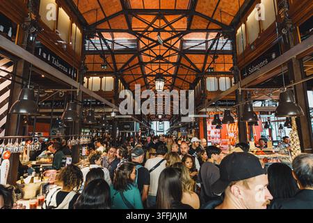 Madrid, Spanien: 7. Apr. 2025 – Eine dichte Menge von Einkäufern und Essern füllt den Mittelgang eines historischen Mercado de San Miguel in Madrid unter einem orn Stockfoto
