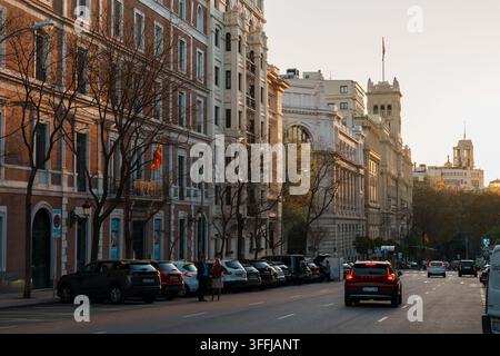Madrid, Spanien: 7. Apr. 2025 – Eine Reihe kunstvoller historischer Gebäude leuchtet im warmen Abendlicht entlang einer breiten Madrider Straße, mit geparkten Autos, die die Kurve säumen Stockfoto