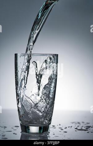 Putzen von erfrischendem Frische-Trinkwasser auf sauberem Transperenzglas in Studiohinterleuchtung Stockfoto
