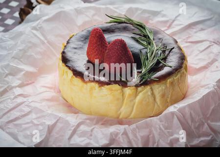 Ein baskischer Käsekuchen mit Erdbeere und Rosmarin, serviert auf einem Gericht mit zerknittertem Papier Stockfoto