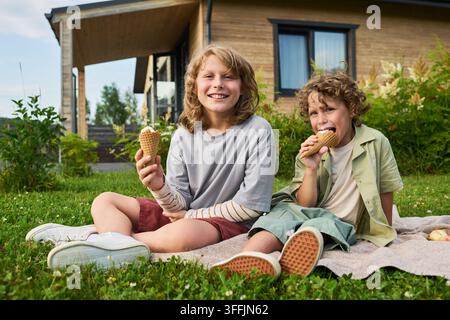 Porträt von glücklichen Kindern, die draußen auf der Wiese Eis essen Stockfoto