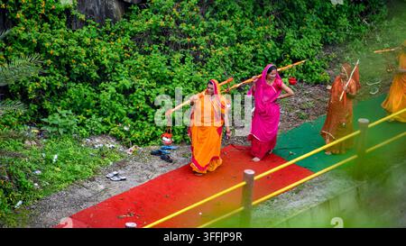 Indische Frauen tragen traditionelles Kavad auf ihren Schultern während einer religiösen Pilgerreise und gehen dabei eine Straße entlang als Teil einer Andachtsreise. Stockfoto
