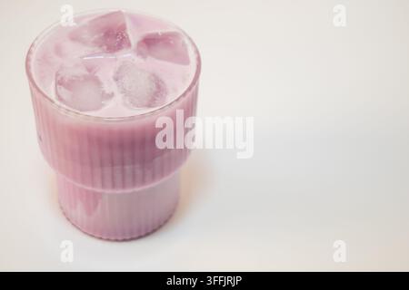 Rosa Matcha mit Eiswürfeln, serviert in einem klaren Glas auf einem hellen Hintergrund mit natürlichem Licht und einer sauberen minimalistischen Komposition Stockfoto