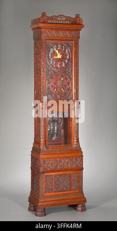 Hohe Uhr. ca. 1880, Hersteller: Tiffany & Co. (Amerika, New York, gegr. 1837) Amerika, New York, Material: Mahagoni, Teak mit Zifferblättern aus vergoldetem und patiniertem Metall, Glas. Maße: Gesamt: 247,3 x 66 x 36,5 cm. Gewicht: 108,862 kg Im Jahr 1879 schloss sich Louis Comfort Tiffany mehreren anderen Handwerkern an, um eine Innenarchitekturfirma namens Associated Artists zu gründen. Das Unternehmen war sehr einflussreich bei der Forderung nach einer Ablehnung historischer Stile zugunsten der neuen Mode aus eklektischeren Inspirationsquellen, einschließlich der islamischen Welt und Japans. Einer von Tiffanys Partnern, Lockwood De Forest, Stockfoto