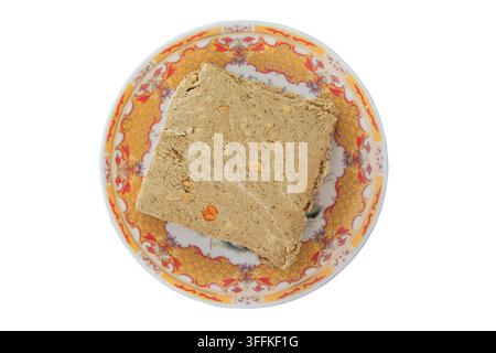 Halwa mit Erdnüssen auf einem Keramikteller isoliert auf weißem Hintergrund. Sonnenblumenhalwa. Oberansicht. Süßes Dessert auf einem Teller im orientalischen Stil. Stockfoto