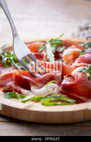 Gabel, die auf einem Holztisch geschnittenen Serrano-Schinken aufnimmt Stockfoto