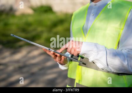 Bauprofi verwendet ein Tablet und trägt dabei eine Warnweste an einer Baustelle im Freien. Digitale Bauprojektleitung, Feldinspektion a Stockfoto