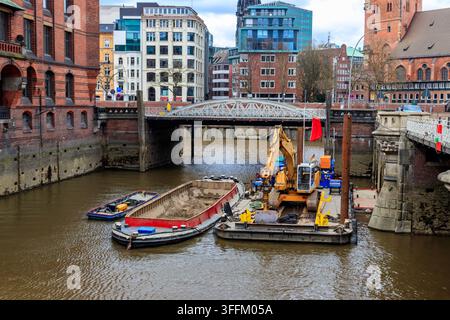 Gelber hydraulischer Bagger auf einer Baustelle, der Restaurierungsarbeiten im Kanal des historischen Speicherstadt-Viertels in Hamburg durchführt, Ge Stockfoto
