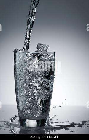 Erfrischende Frische, die Wasser in ein volles, sauberes, durchsichtiges Glas gießt, mit vielen spritzenden Wasser und Blasen im Studio-Rücklicht Stockfoto