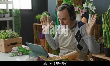 Mann mit Kopfhörern lächelt, Hand auf Tablet, das Tulpen im Blumenladen des Studios arrangiert; Bastelzufriedenheit. Stockfoto